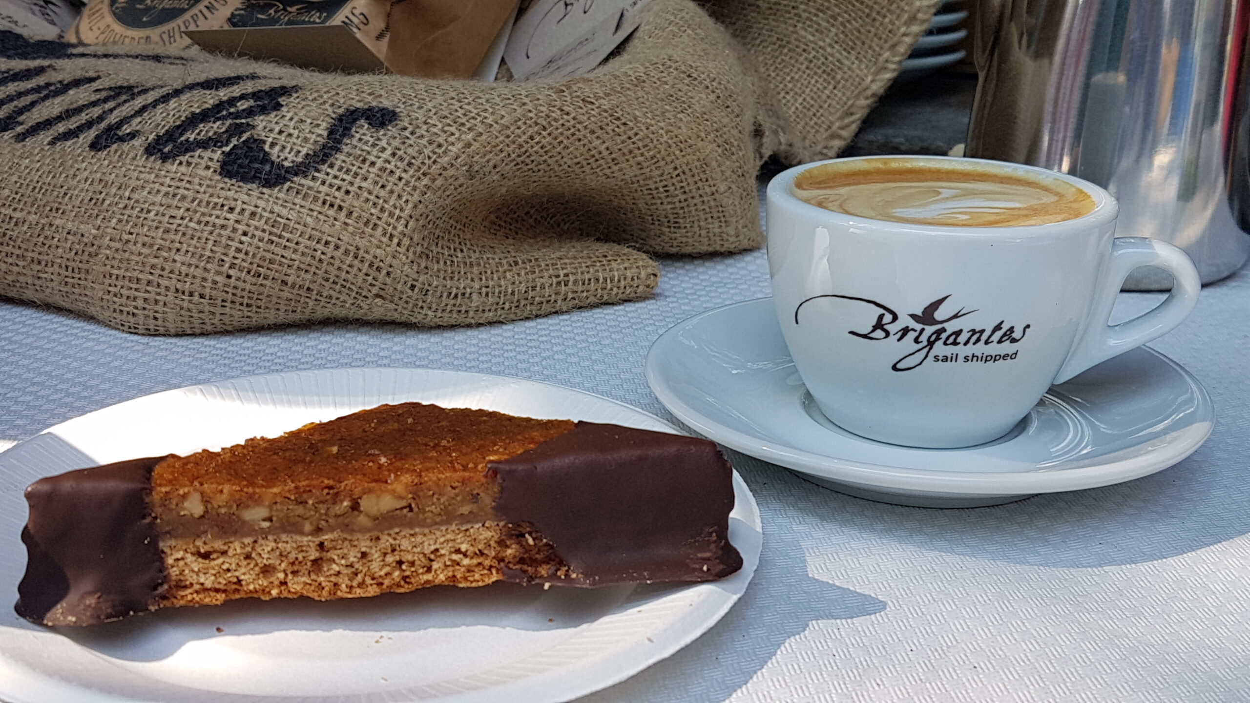 Kaffee und ein Kuchenstück vor einem Jutesack im Freien.